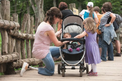 Vrouw met prothesevoet Trias van Ottobock knielt bij kinderwagen van haar kind