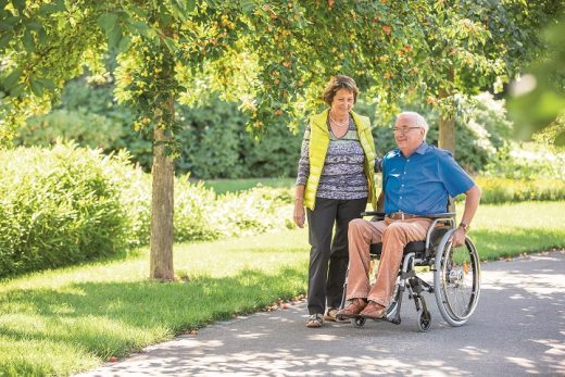 Een man in rolstoel is samen met zijn vrouw buiten voor een ommetje